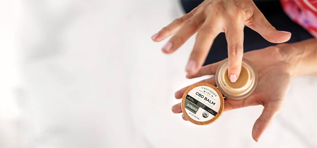 Um frasco aberto de bálsamo Cbd Premium mostrando o início da aplicação tópica de cuidados com a pele pelo usuário final.